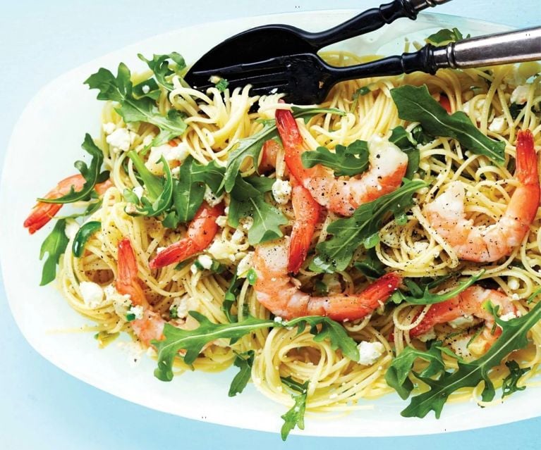 Spaghetti with shrimp and arugula topped with feta cheese, served on a white oval dish with a fork and spoon