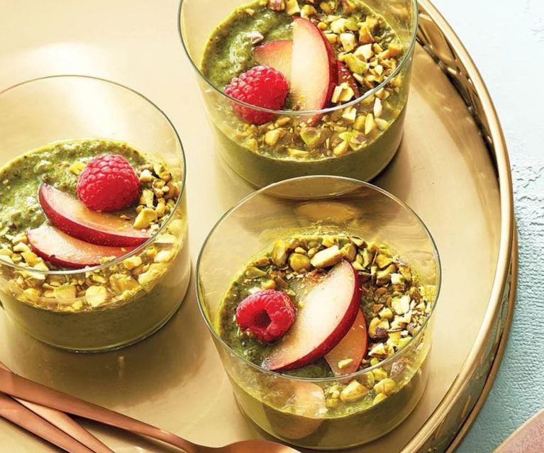 Three glasses with a green chia pudding topped with chopped nuts and fruit