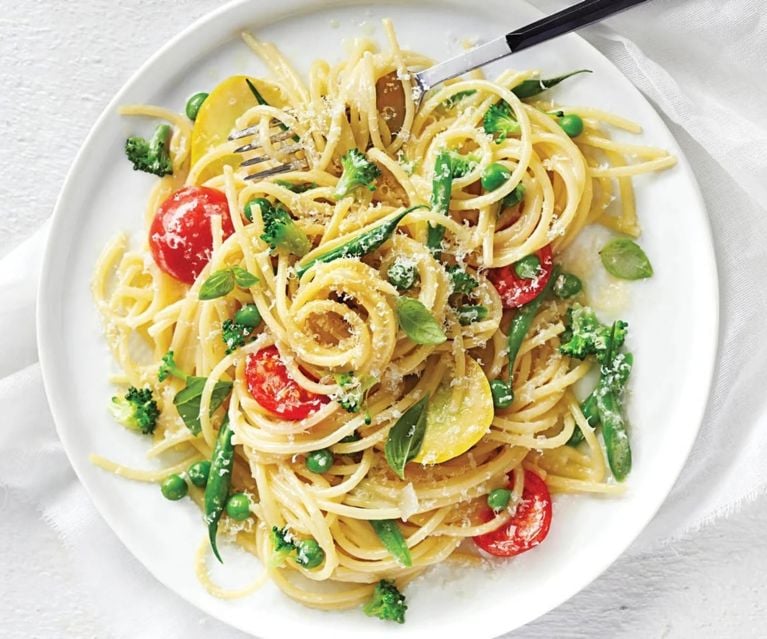 A white plate with spaghetti cooked with cherry tomatoes and green vegetables, topped with grated cheese and served with a fork