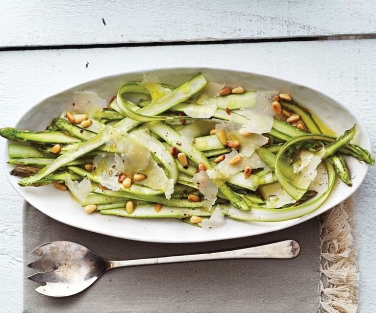 A white oval dish with a salad of shaved asparagus, peas and pine nuts