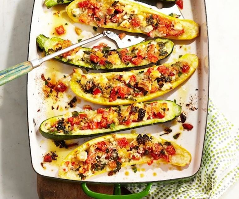 Halved zucchini 'boats' filled with tomatoes and feta in a green baking dish with a serving spatula