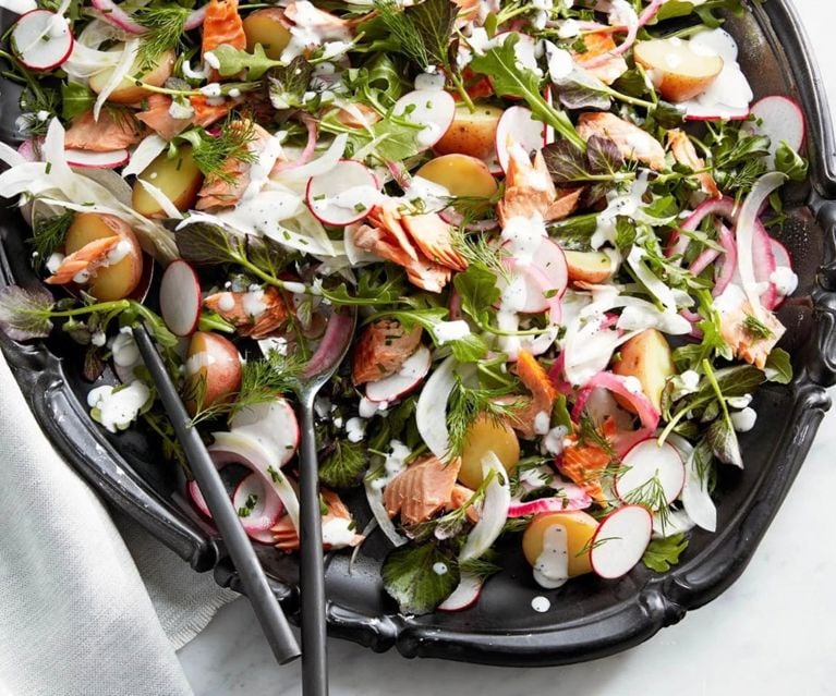A mixed salad with potatoes, fish, fennel, radishes and horseradish served on an ornate black platter