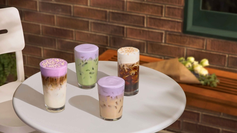 Four new spring Starbucks drinks, including the Iced Lavender Cream Chai Latte, on a white table.