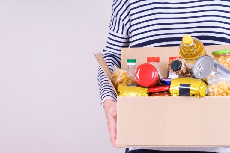 A woman in a striped shirt holding a box of groceries in a post about the Canada Groceries and Essentials Benefit