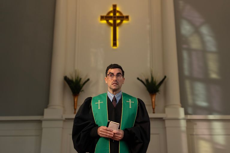 A man dressed as a priest standing under a cross in a post about Dan Levy big mistakes