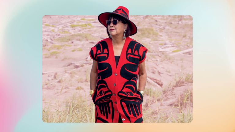 A woman in a red hat and red sleeveless long sweater vest with Haida designs on it used in a post about Dorothy Grant CAFA award.