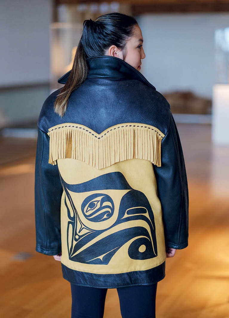 A photo of the back of a woman wearing a black and brown leather fringed jacket with a Haida motif on it in a post about Dorothy Grant CAFA award.