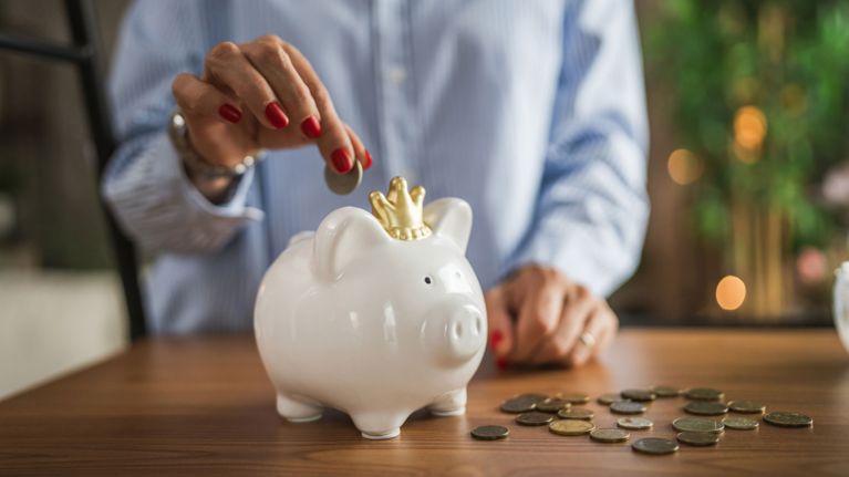 A woman puts money into a piggybank, for a story about how much money you need to retire in Canada.