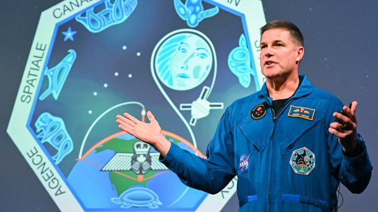 Canadian astronaut Jeremy Hansen speaks in front of a screen displaying the Anishinaabe art patch sewn on his flight suit.