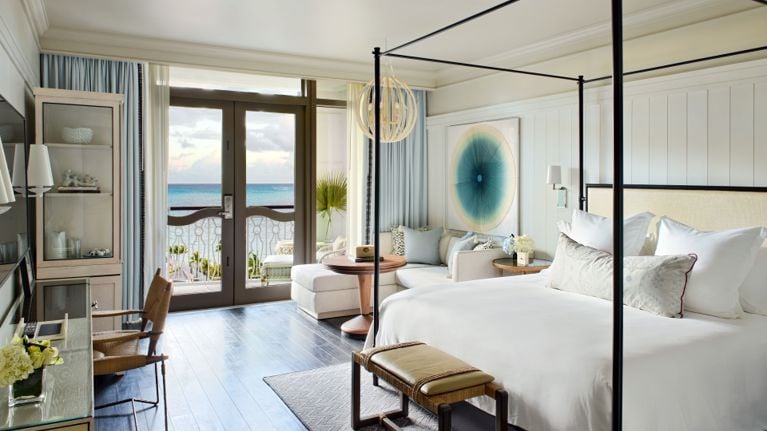 A hotel room with a massive four poster bed and french doors leading to an ocean-view balcony in a post about rosewood baha mar review.