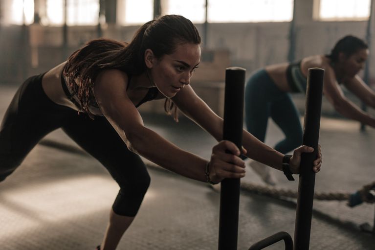 A woman pushing a weighted sled in a post about what is hyrox.