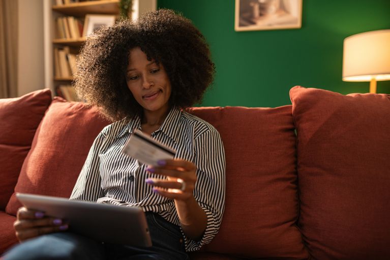 A photo of a woman sitting on a couch with a laptop and a credit card in a post about what is surveillance pricing.