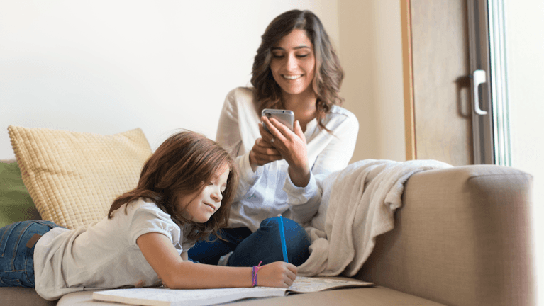 Little girl painting in the living room while her mom is on the phone.