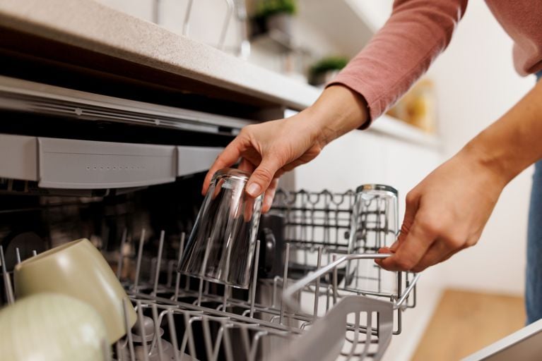 Woman carefully removing clean glasses from the dishwasher in a modern kitchen, engaging in a regular household chore and maintaining a tidy home environment