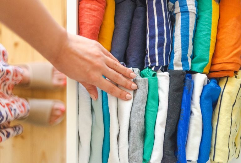 Woman picking colorful clothes from a drawer with neatly folded T-shirts arranged by Konmari method