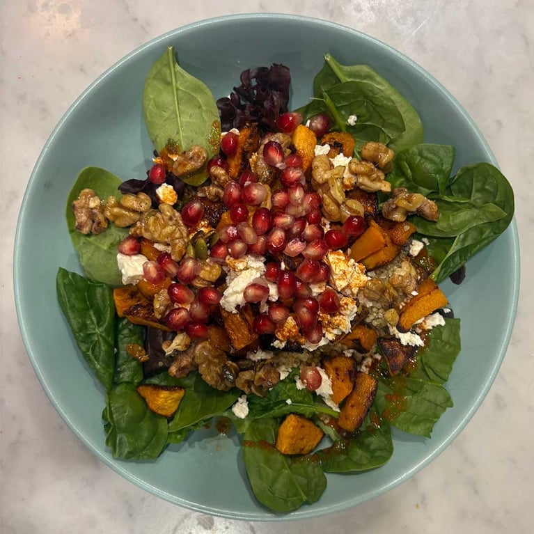 A sage green bowl filled with raosted squash and quinoa salad.