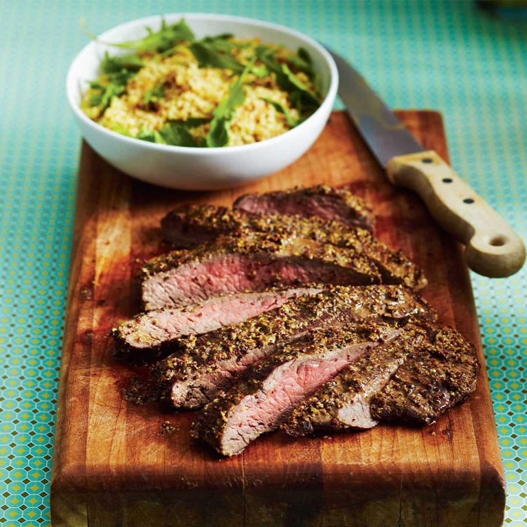 A dijon-crusted flank steak on a cutting board.