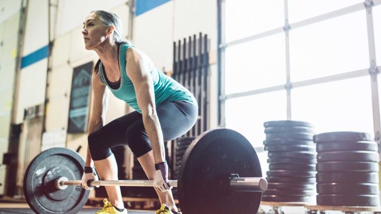 A midlife woman deadlifts in a gym, for a story about exercising during perimenopause.