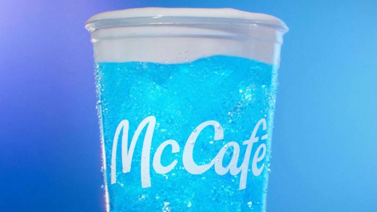 A photo of one of the 3 new McDonald's Crafted Sodas in the flavour Sprite Berry Bliss, a soda with bright blue-raspberry flavour and cold foam on top, on a blue background for an article on a taste test