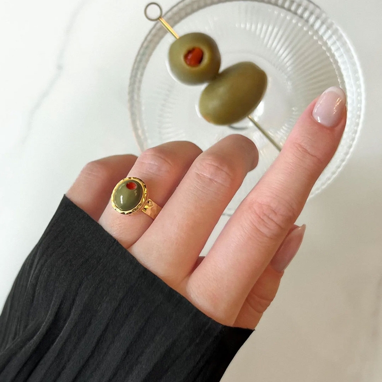 A hand wearing a Fleurs de Fitz Olive Cocktail Ring with a martini glass for an article about the best Mother's Day gifts.