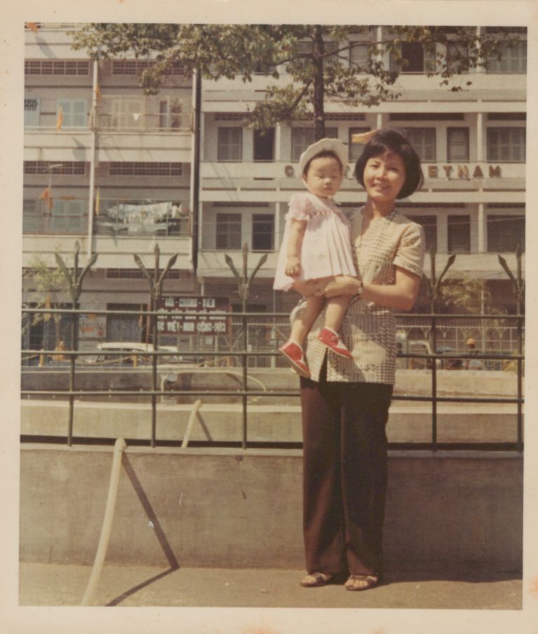 A photo of a woman holding a toddler in a pink dress and red shoes in a post about mothers day tattoo.
