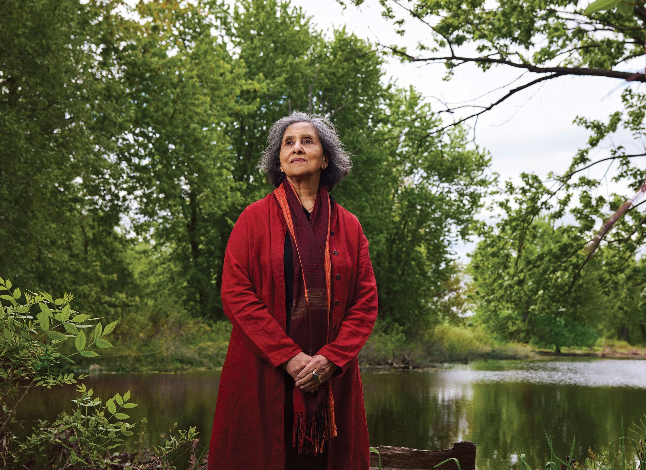 A photo of a woman, Farhat Rehman, wearing red and posing in front of trees and water. Farhat's son, Ahmed, is serving a life sentence in prison.