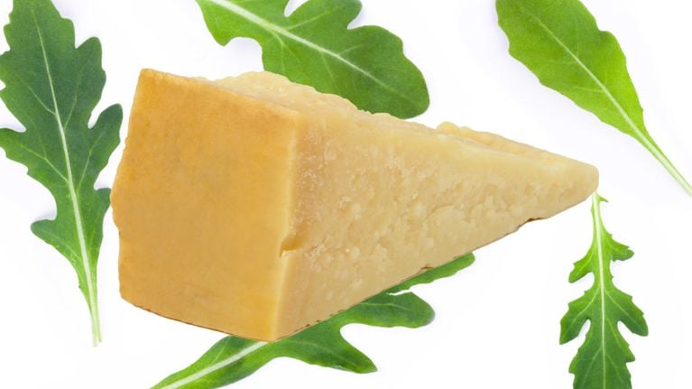 A block of parmesan on top of a arugula leaf background in a post on arugula-for-parmesan-swap