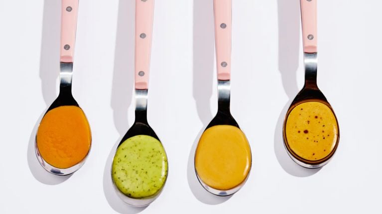 Four pink spoons with Mandy’s salad dressings on them, which are now made with olive oil.