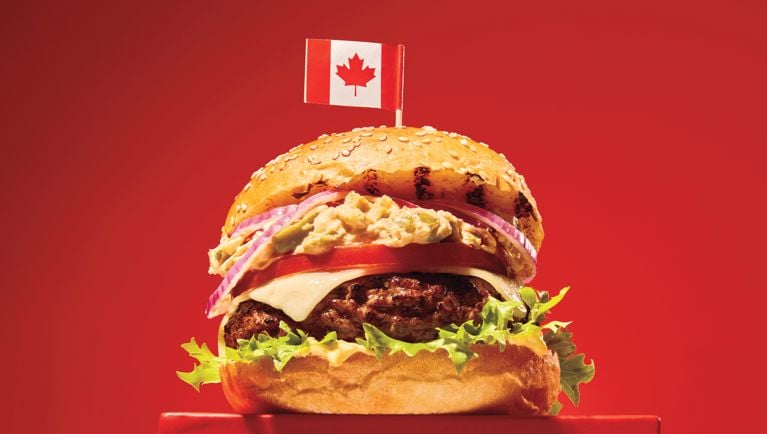 An olive burger hamburger with a canadian flag on the top bun on a red background.